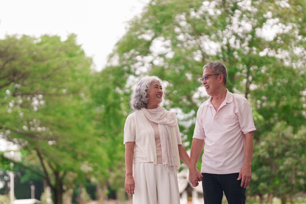 Asian senior couple walking park holding hands smiling healthy active retirement lifestyle bonding outdoors green nature happy together mature relationship journey