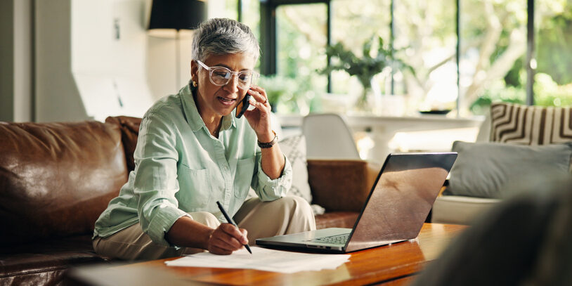 Phone call, laptop and mature woman writing notes for pension, planning and funds in home. Computer, cellphone and senior female person with discussion for investment document or account update